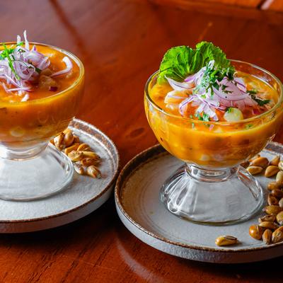 Two cups of citrus ceviche juice with bits of fish topped with white corn and corn nut.