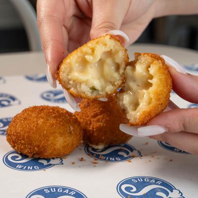 Hands pulling apart a mac and cheese ball on parchment paper.