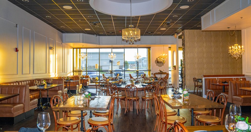 An elegant restaurant interior with tables, chairs, leather booths, chandeliers, and large windows