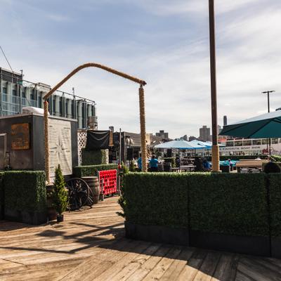 Fenced ourdoor patio with table seating, umbrellas and harbor views.
