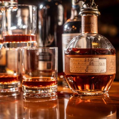 A bourbon bottle and glasses filled with amber liquid sit on a wooden surface.