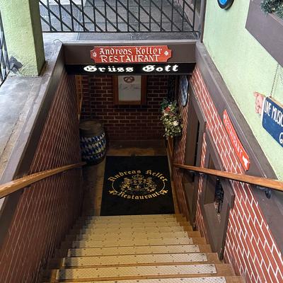 Stairs leading down to Andreas Keller Restaurant, featuring a sign and a decorative rug.