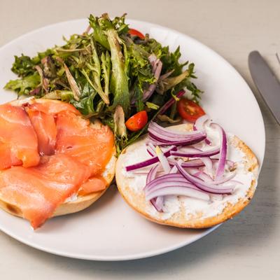Lox bagel with cream and red onion, served alongside a mixed green salad.