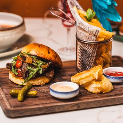 Sveta's Burger served with fries, sauce dishes, and pickle on a wooden board.