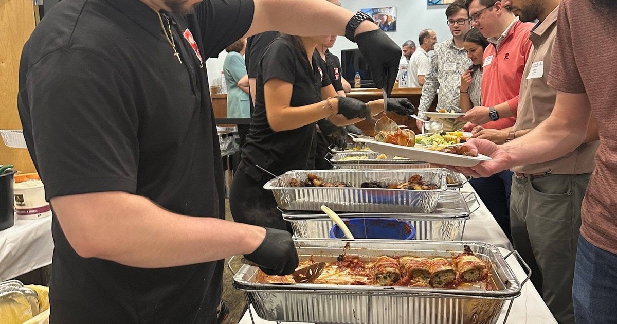 Buffet-style catering setup featuring staff serving food from aluminum trays