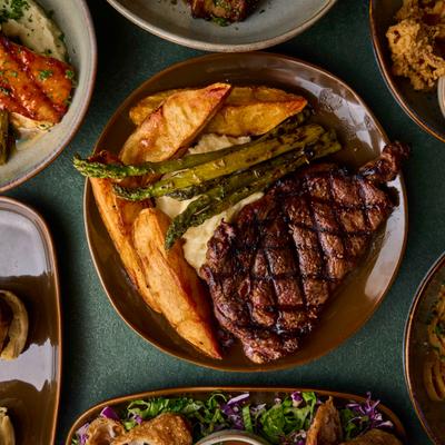A grilled steak dinner with sides of roasted asparagus and potato wedges.