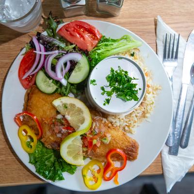 Fried fish filets with rice, mixed greens, tomato, red onion, pepper slices, and a sauce.