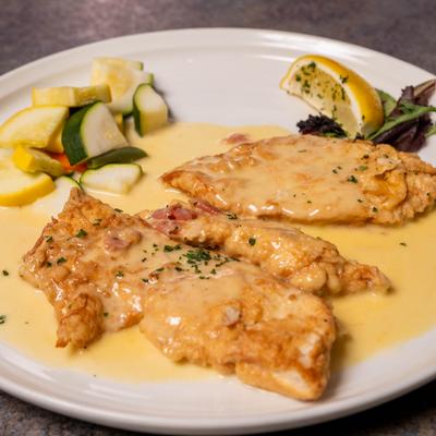 Chicken Francese served with vegetables and a lemon wedge.