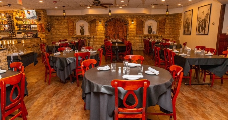 A rustic restaurant interior with round tables, red chairs, and exposed brick walls