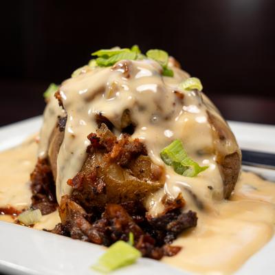 Close-up of a loaded baked potato topped with bacon, creamy sauce and scallions.