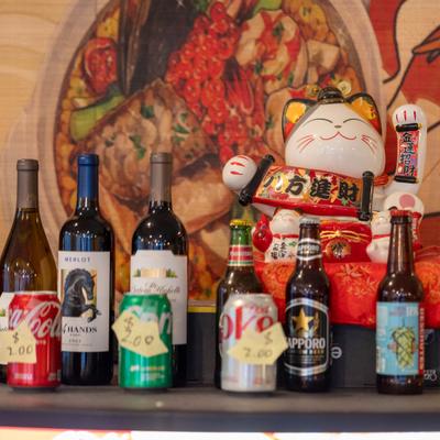 Lucky cat figurine behind assorted soda cans and wine and beer bottles.