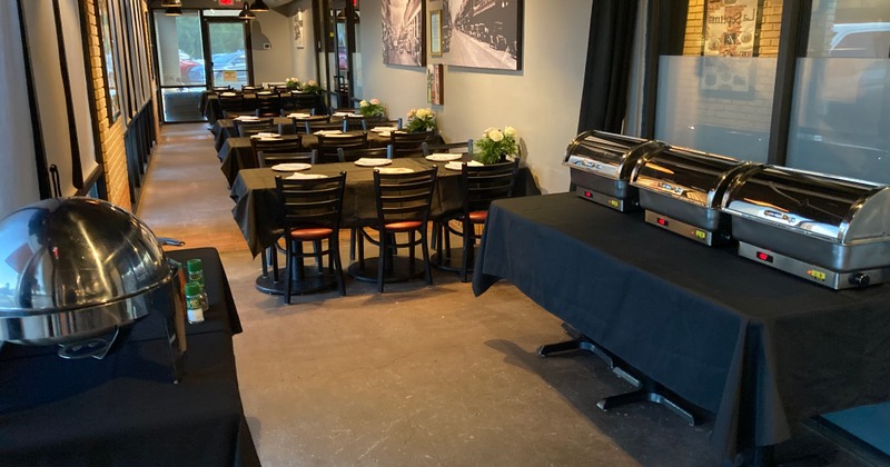 The room features long tables set for dining, Chafing dishes are visible on separate tables