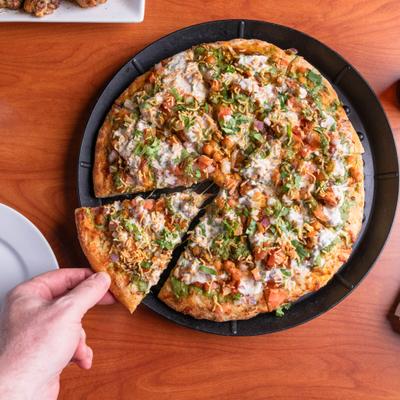 Hand taking a slice of Samosa Chaat pizza.