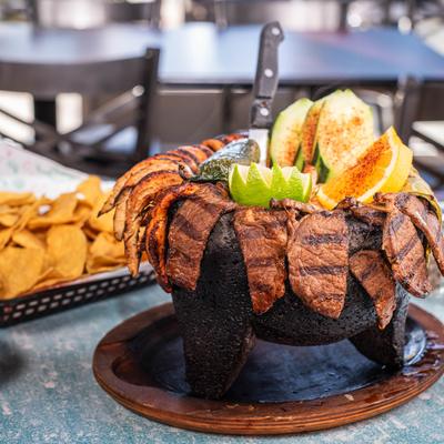 Grilled steak and chicken molcajete with cucumber slices, lime, and jalapeno.