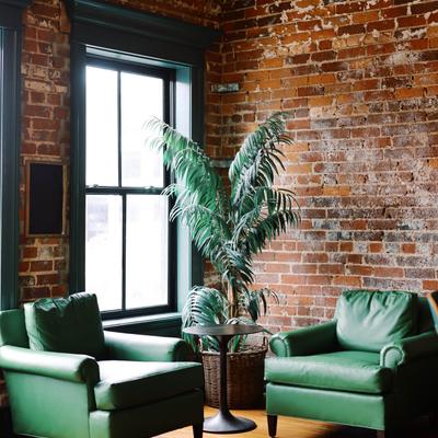 Lounge corner with green leather chairs, potted plant, and brick walls.