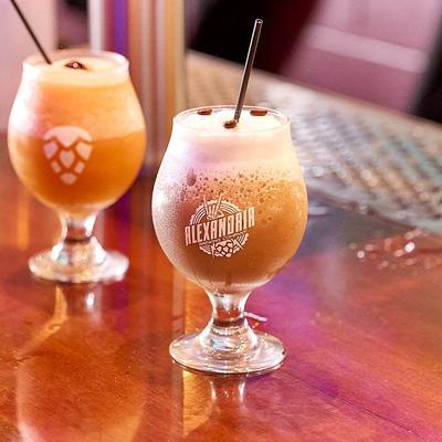 Two branded glasses hold foamy craft beers on a shiny bar counter..