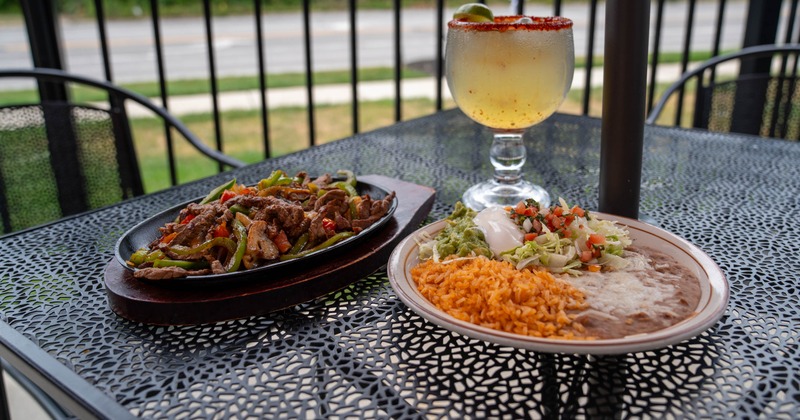 Steak fajitas served with a separate plate of sides and a Margarita cocktail