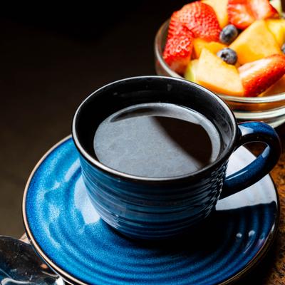 Cup of black coffee on saucer, alongside fruit salad.