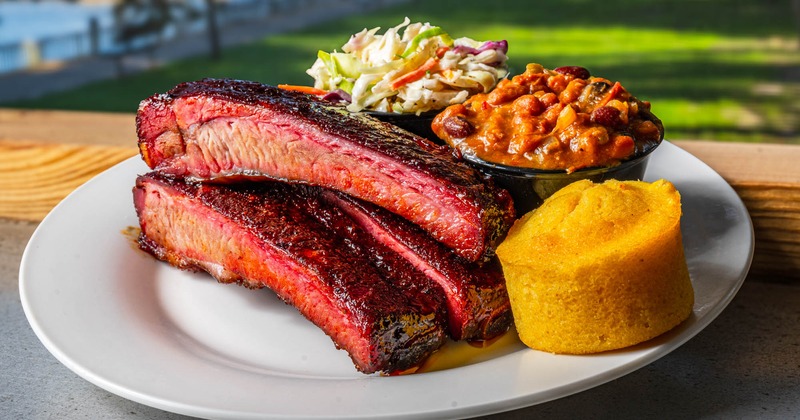 Rib lunch plate with sides of coleslaw, baked beans, cornbread ,served on a table outdoors