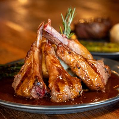 Grilled lamb chops arranged upright, glazed with brown sauce; mashed potatoes and grilled asparagus.