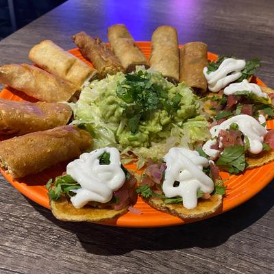 Mini flautas and taquitos on a plate with guacamole and sour cream.