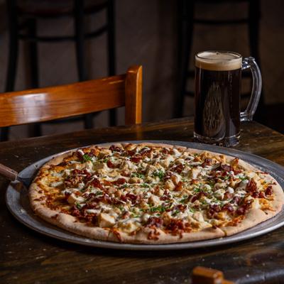Pizza topped with chicken, bacon, and herbs served with a pint of dark beer.