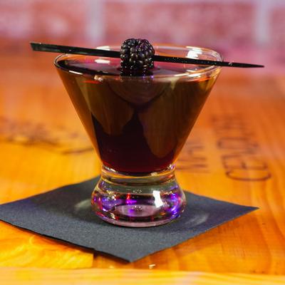 Dark berry cocktail garnished with a blackberry on a wooden table.