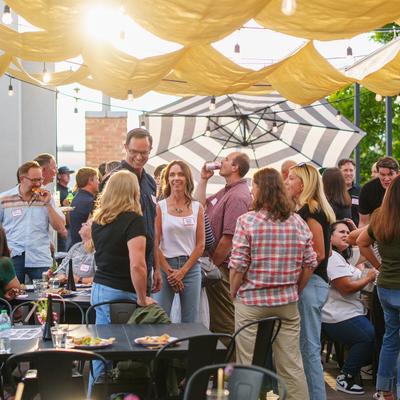 Sunlit rooftop gathering with people talking under fabric canopy shades.