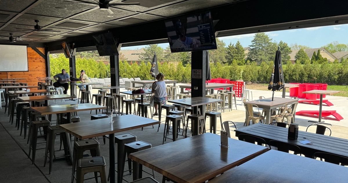 A covered patio with TVs and a view of trees in daylight