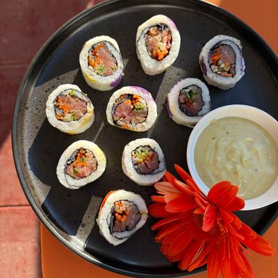 Tuna maki rolls with a bowl of creamy green sauce and flower garnish.