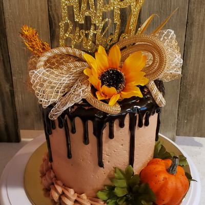 Chocolate drip cake with a sunflower, gold ribbon, and Happy Birthday topper.