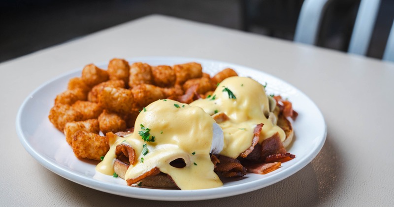 Bacon Eggs Benedict served with tater tots on the side