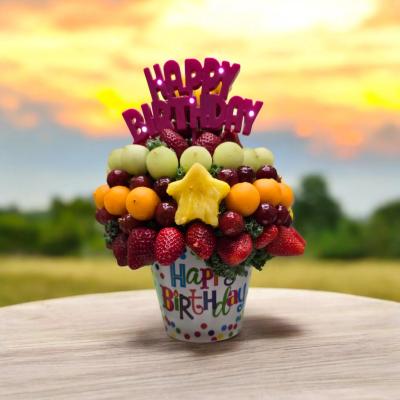 Colorful fruit bouquet in a Happy Birthday pot, sunset sky background.