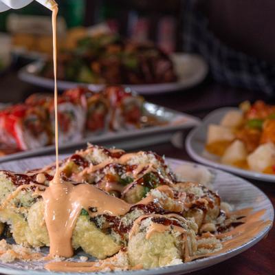 Tempura sushi rolls being drizzled with sauce.