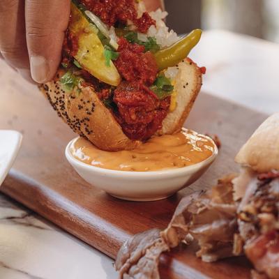 A hand dipping a hot dog.