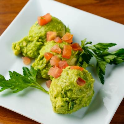 Scoops of guacamole topped with diced tomatoes and cilantro.