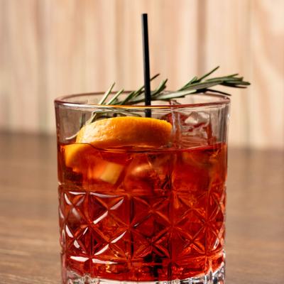 Negroni cocktail garnished with a orange peel and rosemary spring.