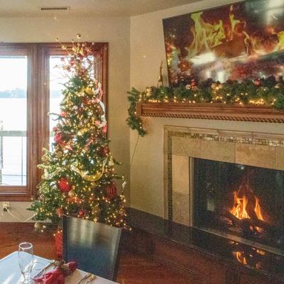 Room with a decorated Christmas tree by a window, a lit fireplace, and garland on the mantel.