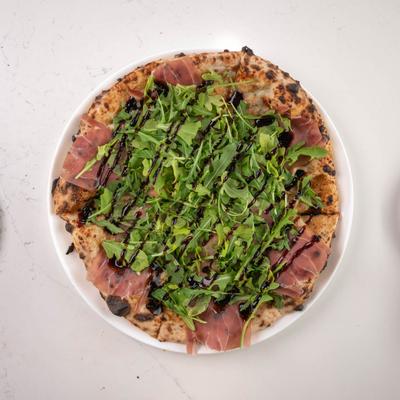 A pizza with fig jam, gorgonzola, prosciutto, arugula, and balsamic glaze.