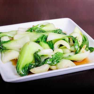 Stir-fried bok choy on a white rectangular plate with light sauce.