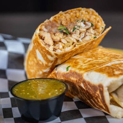 Burritos cut in half on a plate with green salsa.