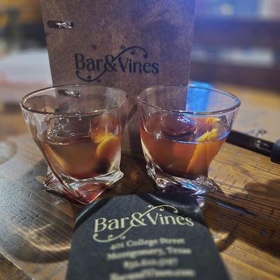 Two Old Fashioned cocktails served on a bar with menus.