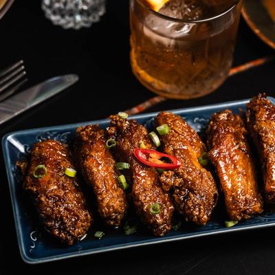 A plate of glazed chicken wings garnished with green onions and a slice of red chili.