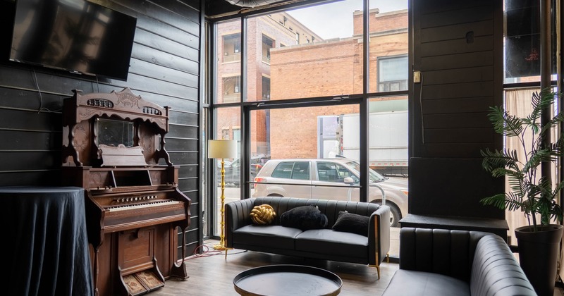 Industrial-style lounge with sofas, vintage piano, and large windows
