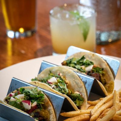 Tacos served with French fries and a cocktail in a restaurant setting.