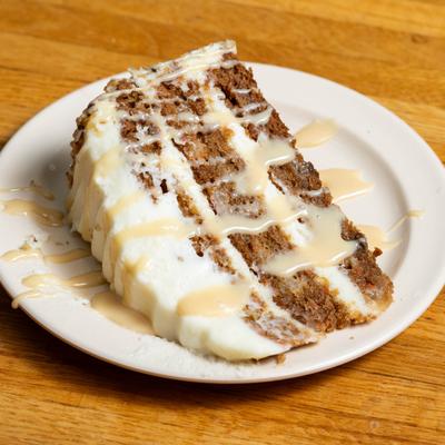 Carrot cake slice drizzled with creamy sauce.