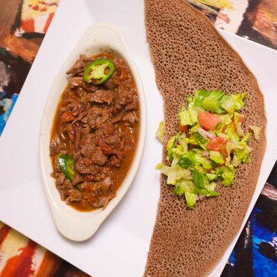 Plate of beef stew served with injera and salad on the side.