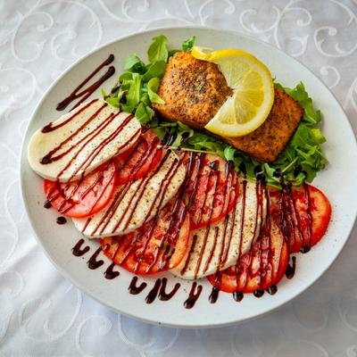 Salmon fillet served on a bed of arugula alongside Caprese salad drizzled with a balsamic glaze.