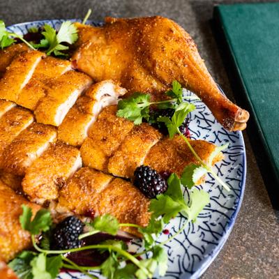 Sliced roasted poultry on a patterned plate with cilantro and blackberries.