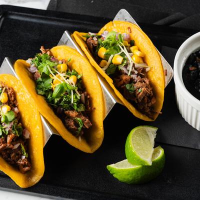 Brisket tacos served with lime slices and black beans.